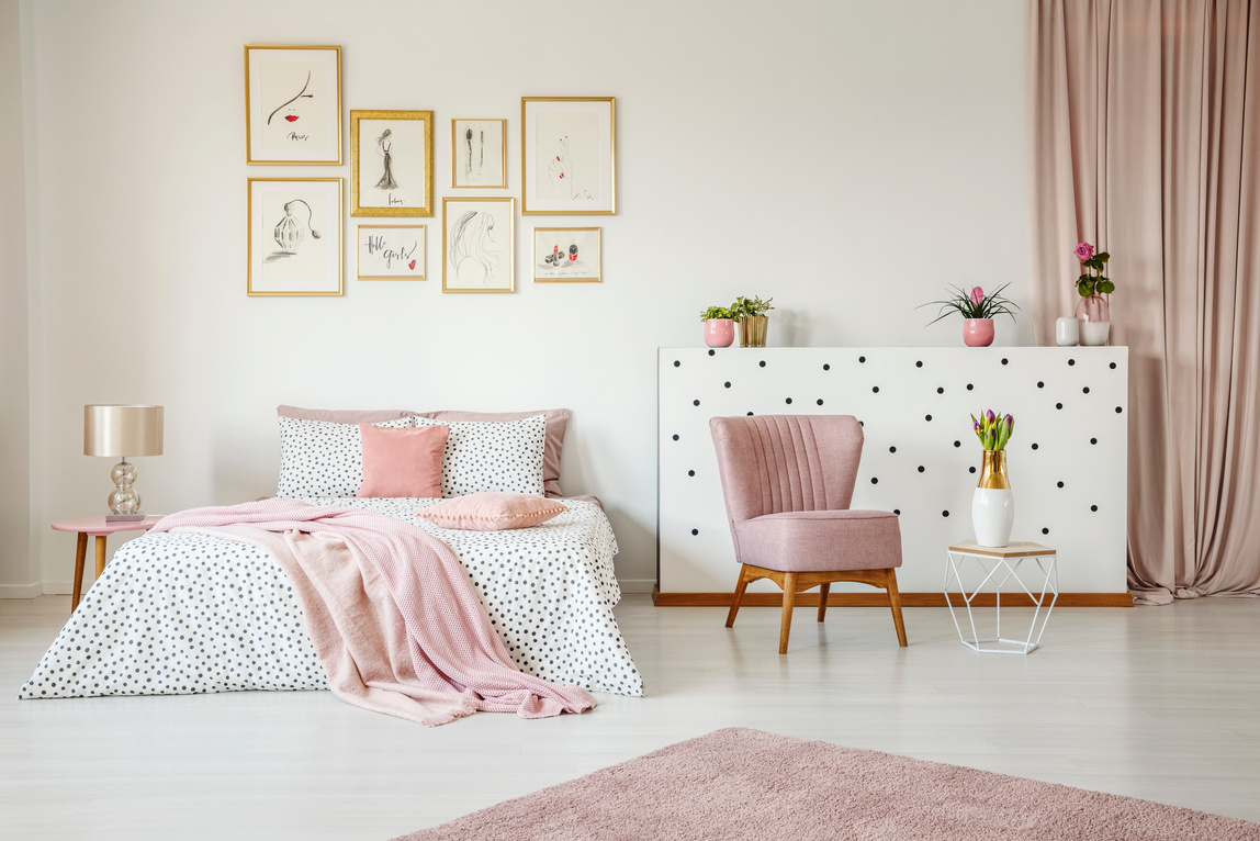 a pink and white bedroom with a bed, chair and pictures on the wall